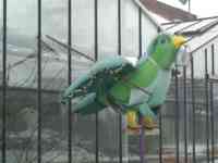 Sculpture of green sparrow with rake, watering can, smock, and boots